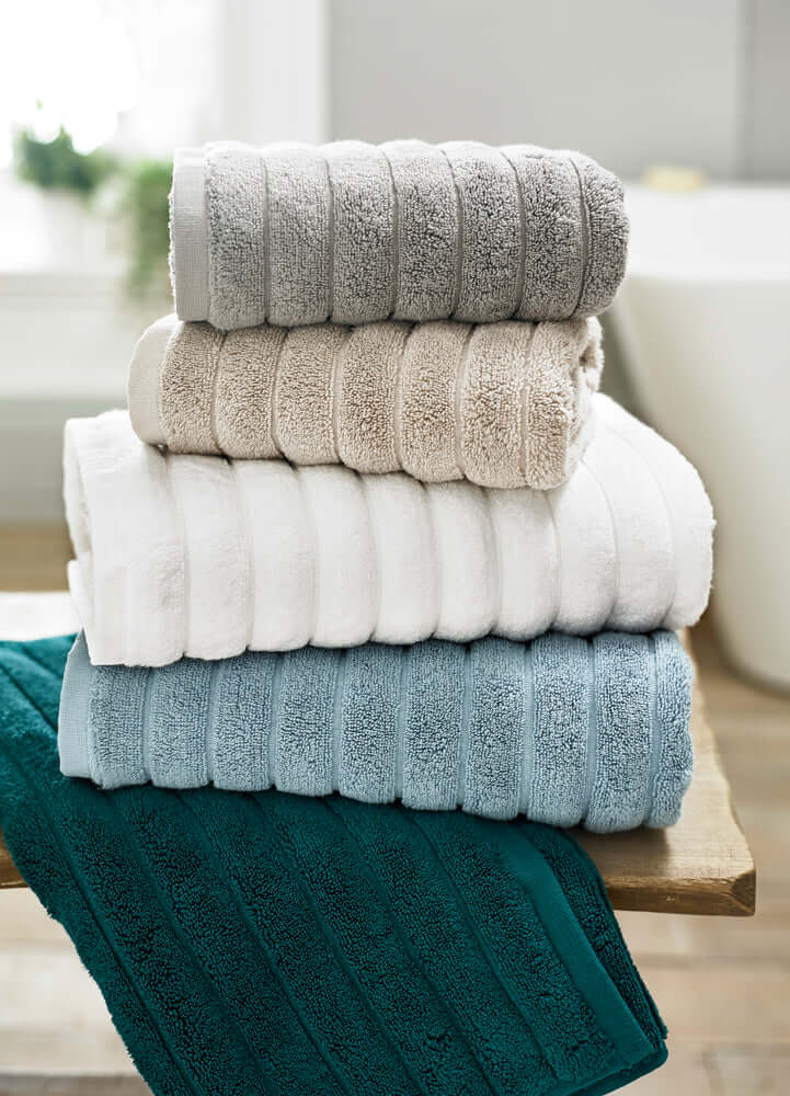 Stack of folded Ribbleton Zerotwist Cotton Towels in beige, gray, blue, and green colors, displaying a ribbed textured pattern.