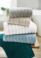 Stack of folded Ribbleton Zerotwist Cotton Towels in beige, gray, blue, and green colors, displaying a ribbed textured pattern.