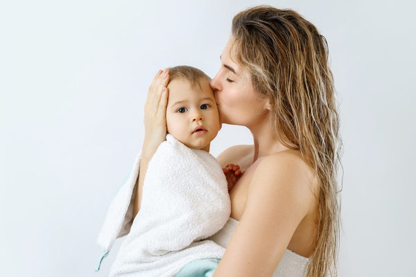 A mum kissing her baby, who is wrapped in a white towel