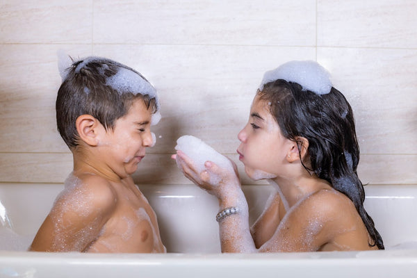 A brother and sister playing with bubbles at bath time