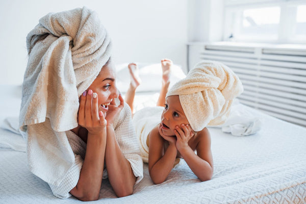 A mum and her daughter laughing with towels wrapped around their hair
